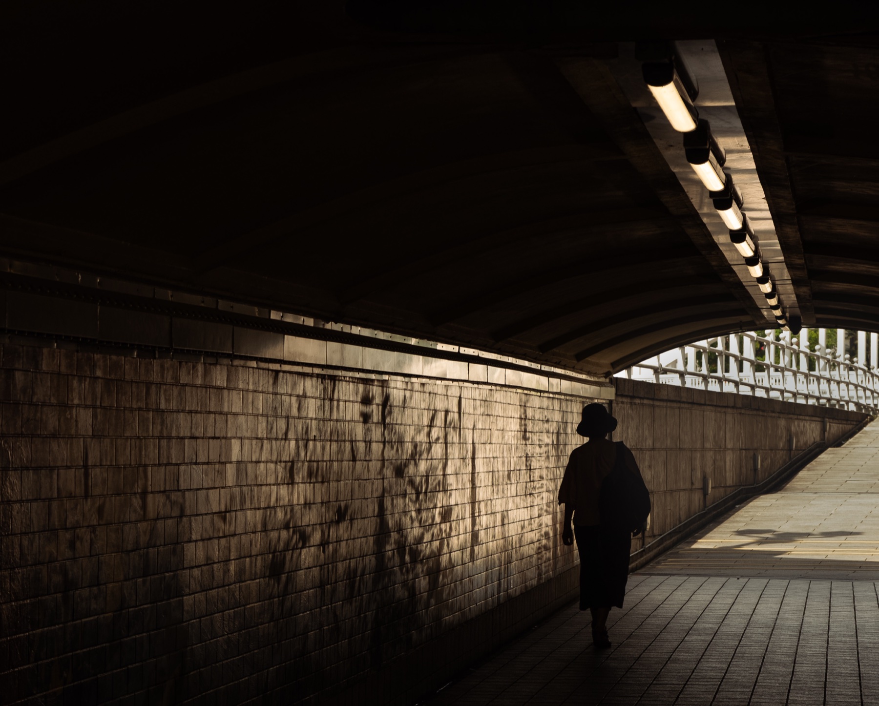 A lone figure walking through a warm-lit underpass