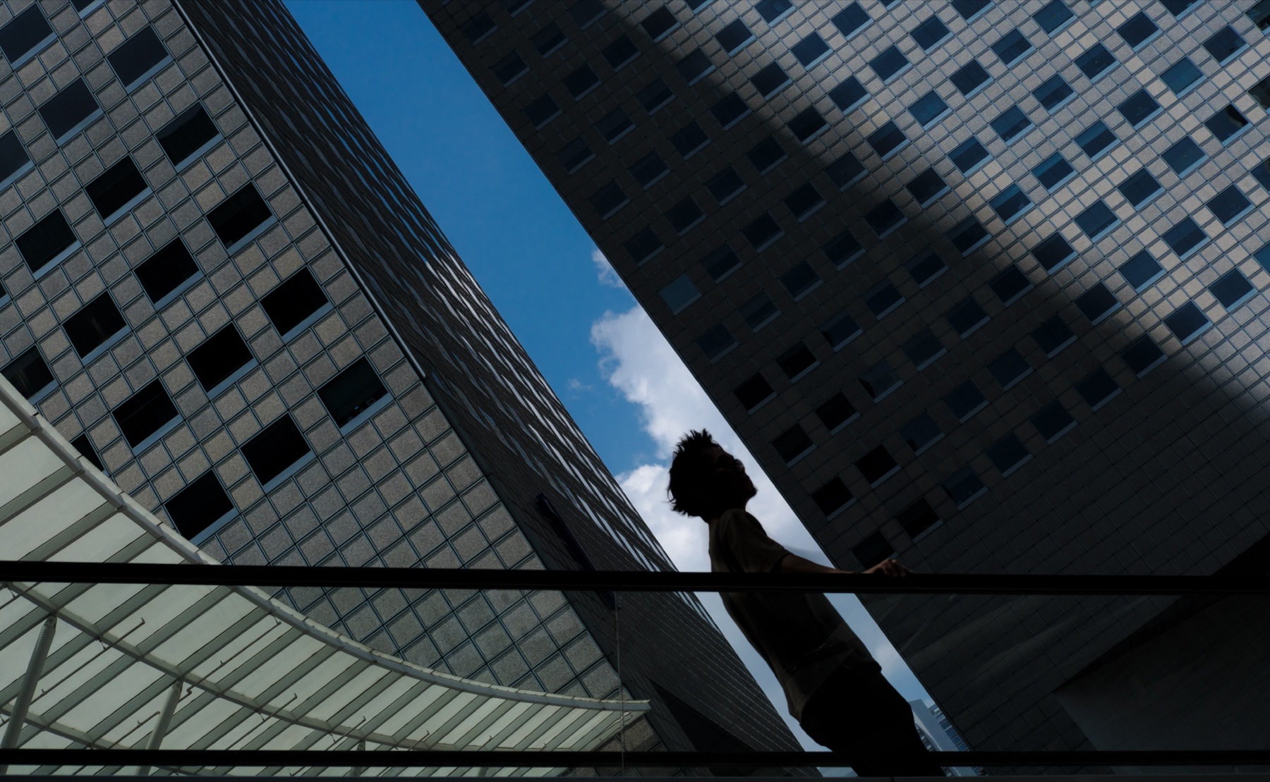 A figure silhouetted against towering skyscrapers and a slice of blue sky