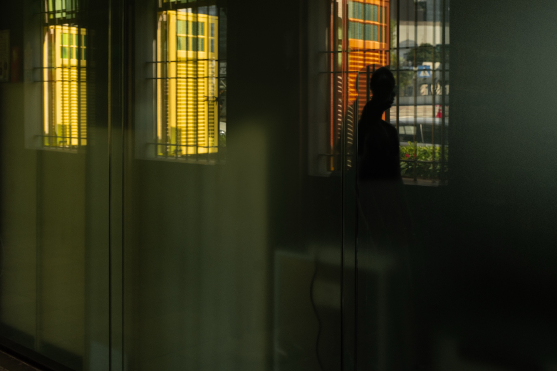 A silhouette behind glass, warm windows glowing in reflection