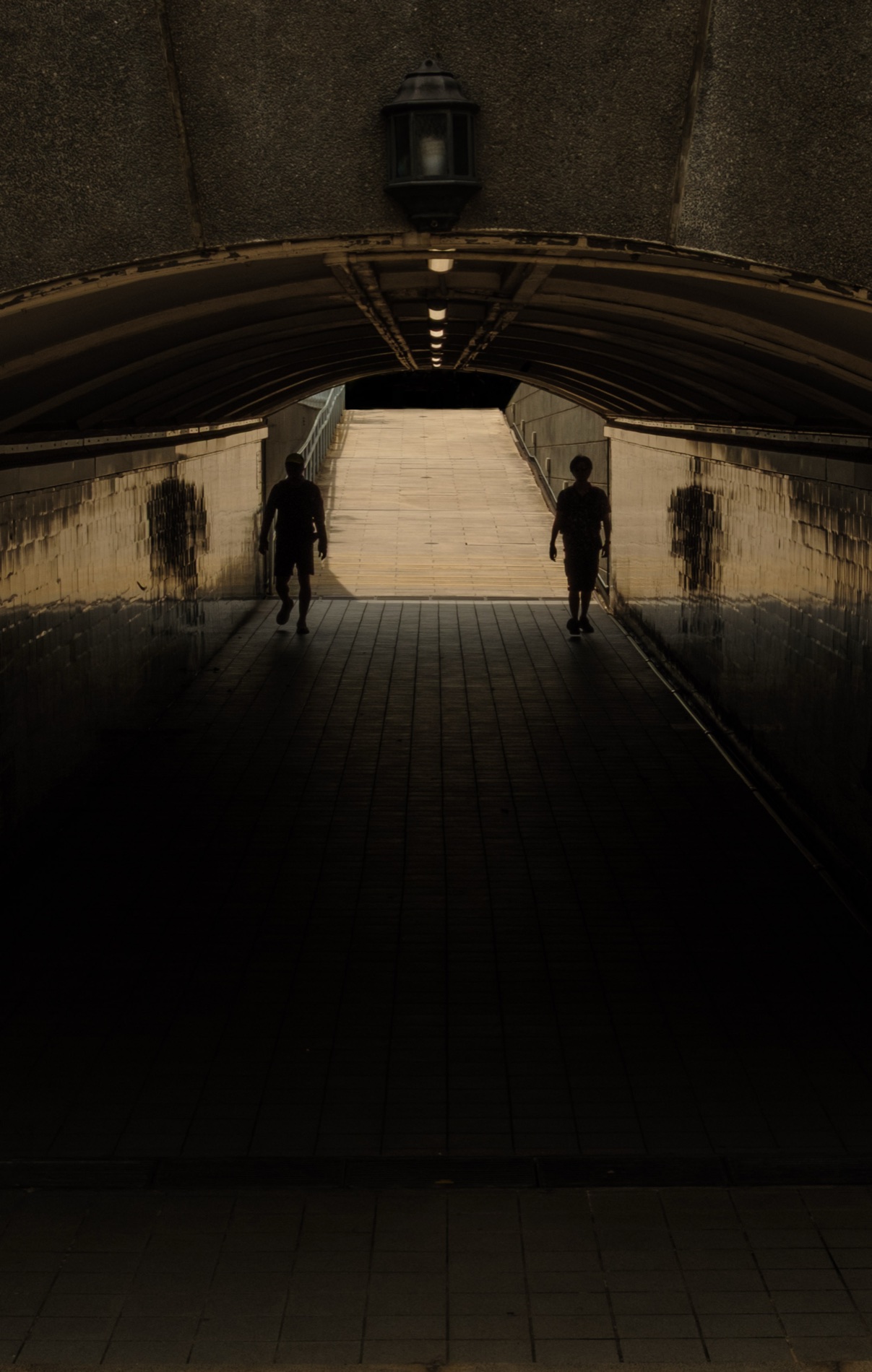 Two figures silhouetted at the lit mouth of an underpass