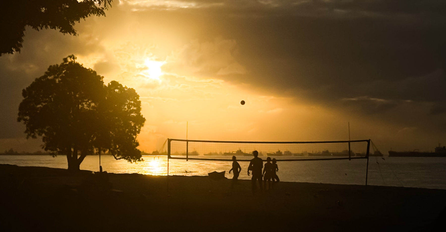 Silhouetted figures playing volleyball against a golden sunset over the sea